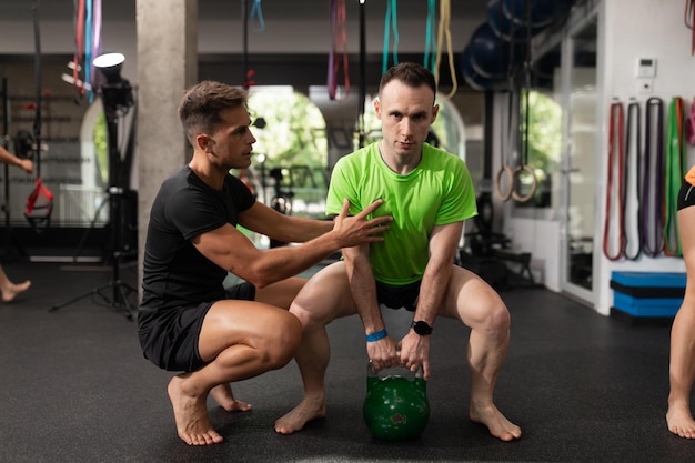 Um treinador ajuda a posição do estagiário durante um exercício de agachamento de sumô com um kettlebell