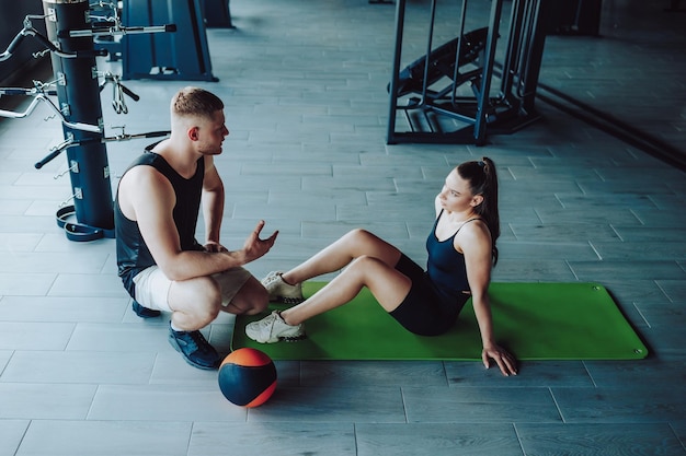 Foto um treinador pessoal é visto tendo uma conversa informativa com uma cliente feminina no ginásio, fornecendo ajuda valiosa e explicando as complexidades de diferentes exercícios