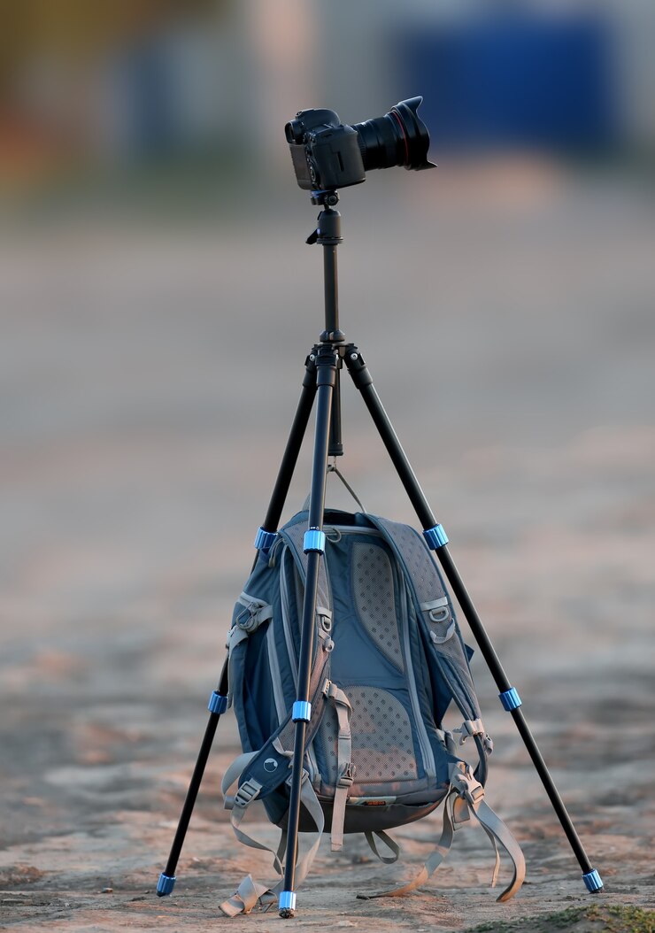Um tripé solitário e uma mochila de fotógrafo pendurada nele são fotografados de manhã cedo em um local vazio