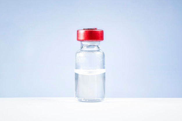 Um tubo de vidro transparente com líquido fica sobre uma mesa branca contra um fundo azul. O conceito de pesquisa laboratorial. A vacina vem em uma garrafa. Um tubo de ensaio para inoculação.