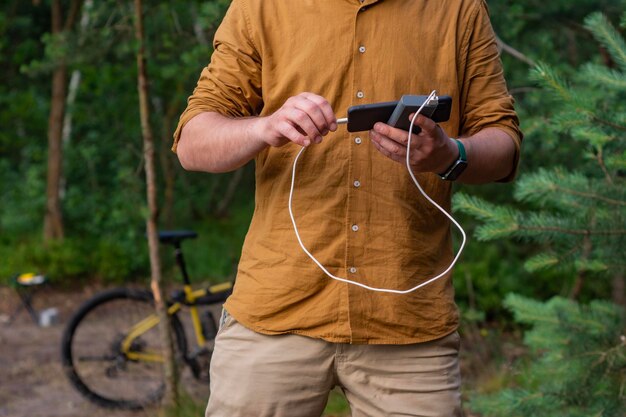 Foto um turista carrega um smartphone com um banco de potência no fundo de uma bicicleta na floresta