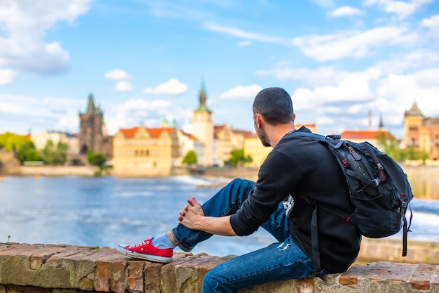 Um turista com uma mochila sentado na margem em praga com vista para o rio moldava