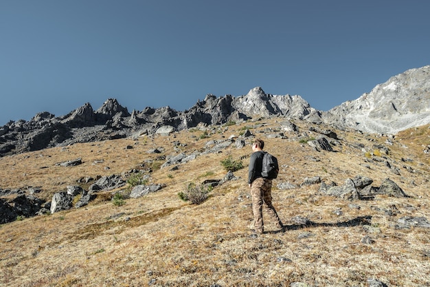 Um turista masculino com uma mochila sobe uma colina até um pico rochoso Motivação e alcançar seus objetivos