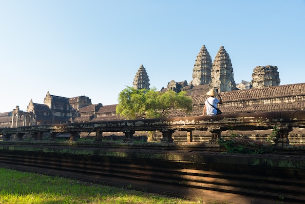 Um turista que visita angkor arruina entre a selva, complexo do templo de angkor wat, destino camboja do curso. mulher com chapéu tradicional, vista traseira.