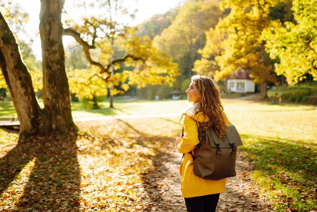 Um turista sorridente com um casaco brilhante caminha por um parque de outono em clima ensolarado Conceito de viagem