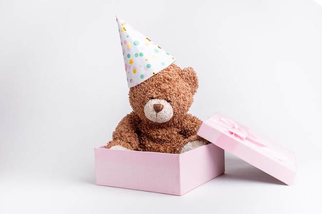 Um ursinho de pelúcia em uma caixa de presente rosa comemora um aniversário em um fundo branco isolado