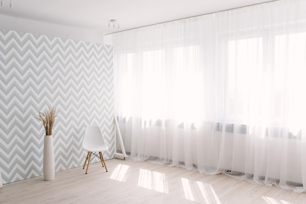 Um vaso branco com plantas secas decorativas ao lado de uma cadeira branca no interior elegante da sala