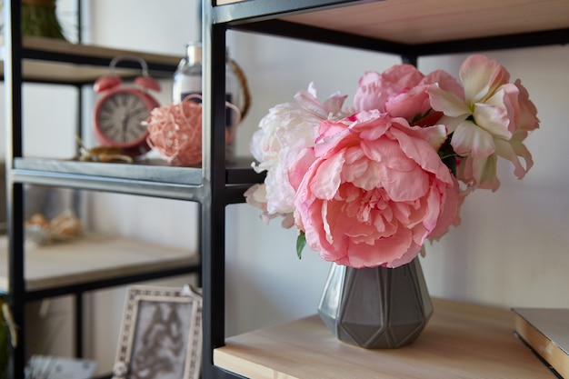 Um vaso com flores cor de rosa com carrinhos despertador em uma prateleira na sala.