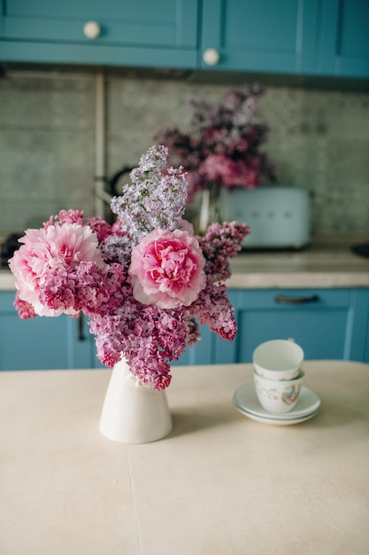 Um vaso de flores em um balcão de cozinha com uma xícara de chá e uma xícara de chá sobre a mesa.