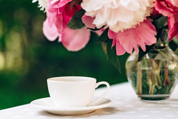 Um vaso de flores peônias perto de uma xícara de café