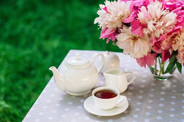 Um vaso de flores peônias perto de uma xícara de chá