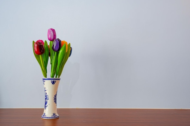 Um vaso de tulipas está sobre uma mesa com fundo branco.