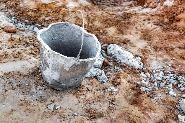 Um velho balde de metal manchado em concreto ou argamassa em um canteiro de obras Ferramenta de construção para concretagem