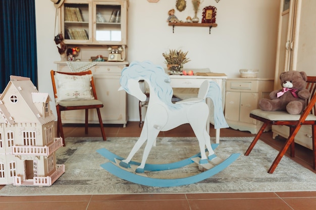 Um velho cavalo de balanço vintage no fundo de um quarto infantil com uma casa de bonecas e antiguidades