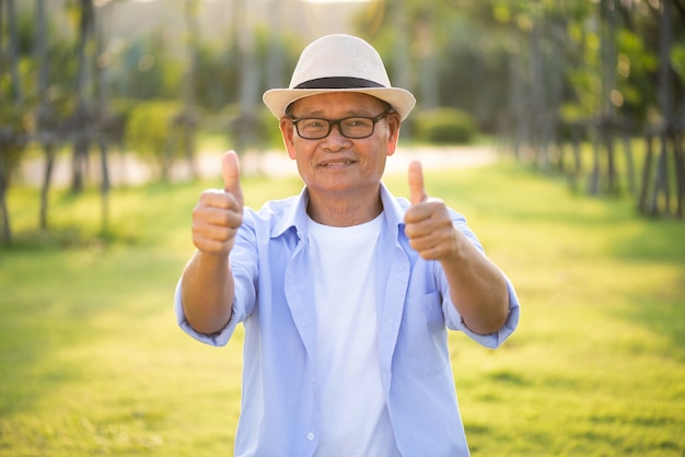 Um velho feliz com polegares para cima sorrindo e rindo no jardim