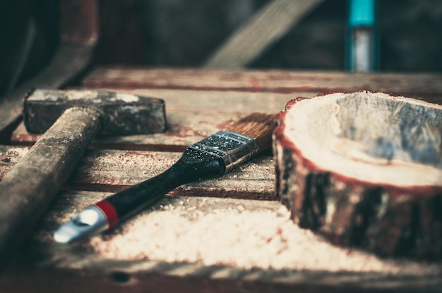 Um velho martelo enferrujado, um pincel e uma viga de pinho redonda com serragem em um banco Suporte de madeira para comida para o conceito de bricolage master class