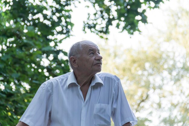 Um velho pensativo de camisa branca está relaxando em uma caminhada no parque