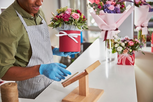 um vendedor de flores afro-americano enviando uma mensagem de texto em um teclado de telefone em um suporte de madeira enquanto guarda um vaso