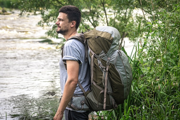 Um viajante com uma grande mochila de caminhada está parado perto do rio.