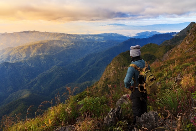 Um viajante no topo da montanha, ele de pé sobre a rocha assistindo um nascer do sol