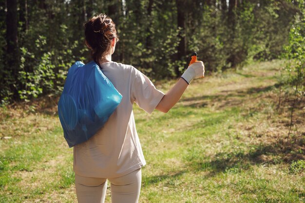 Um voluntário coleta garrafas plásticas na floresta. A menina segura um saco de lixo nas mãos e mostra um gesto com a mão: ótimo, turma. Chamada de conceito para proteger o meio ambiente, o planeta.