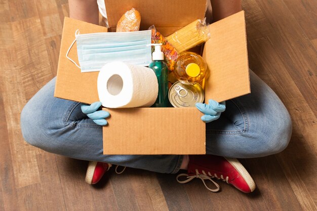 Um voluntário sentado no chão e segurando a caixa de doação com papel higiênico de comida e desinfetante