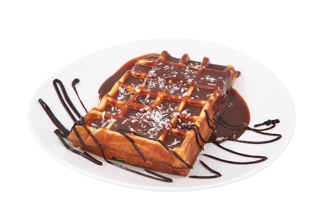 Um waffle belga, derramado chocolate derretido e polvilhado com coco deitado no prato, isolado no fundo branco.