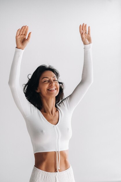 Foto um yogi feminino em roupas brancas com as mãos para cima medita no salão de yoga