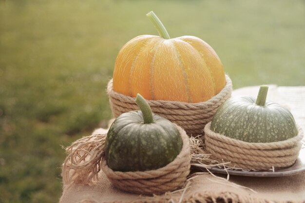 Foto uma abóbora laranja e duas abóbora verde na mesa de madeira decorada estopa e corda. ao ar livre.