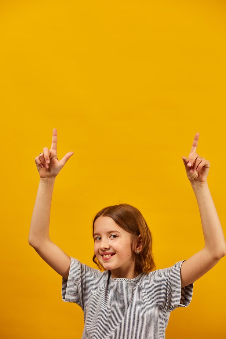 Foto uma adolescente alegre e positiva de dez anos apontando os dedos para cima na área de trabalho isolada no espaço de cópia de estúdio de fundo amarelo para simulação de texto