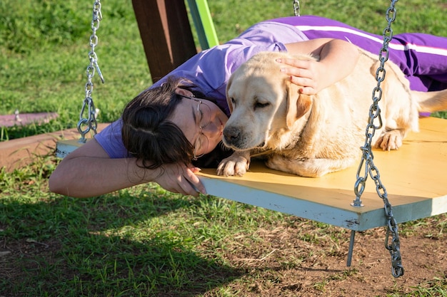 Uma adolescente balança em um balanço com seu velho cachorro Labrador