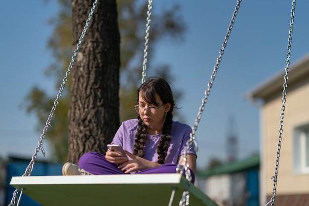 uma adolescente balança em um balanço com um telefone nas mãos, se comunica nas redes sociais