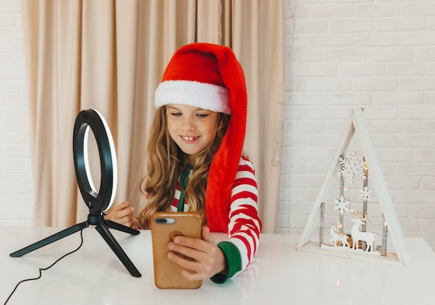 Uma adolescente blogando sobre o Natal. criança blogueira de pijama listrado grava vídeo no telefone.