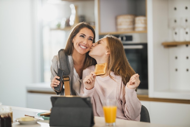 Uma adolescente bonita e sua mãe sorridente se cumprimentam em sua casa enquanto a mãe se prepara para ir trabalhar.