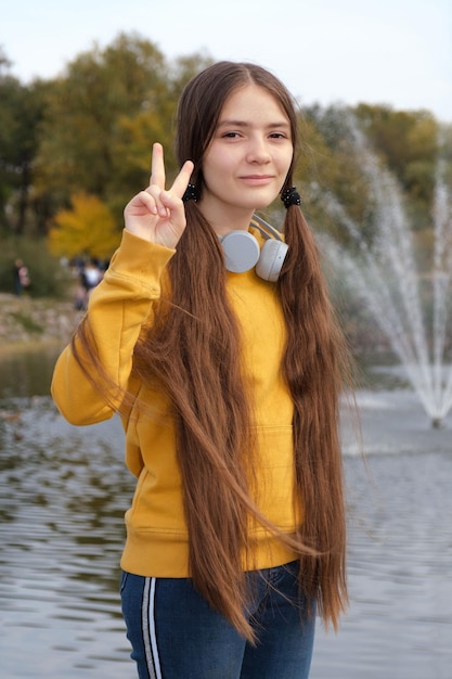 Foto uma adolescente com cabelos compridos e fones de ouvido mostra um gesto de dois dedos.