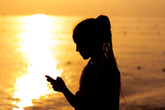 Uma adolescente com um telefone no fundo do mar do pôr-do-sol resto comunicação online verão