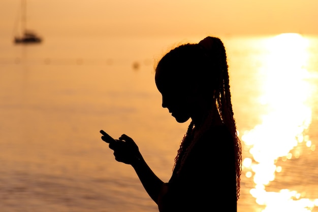 Uma adolescente com um telefone no fundo do mar do pôr-do-sol Resto Comunicação online Verão