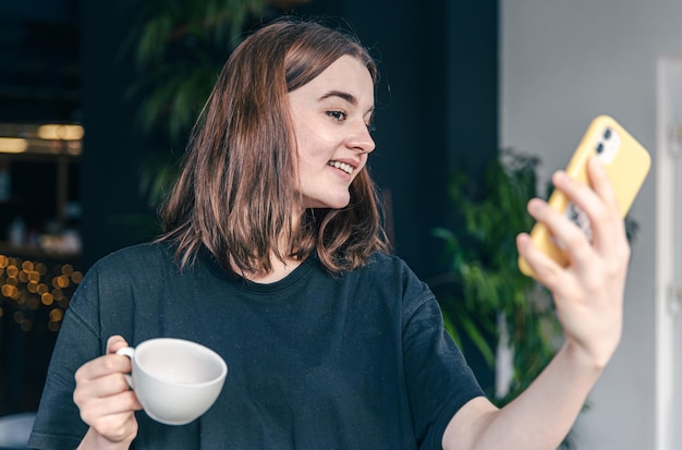 Uma adolescente com uma xícara de chá e um smartphone nas mãos