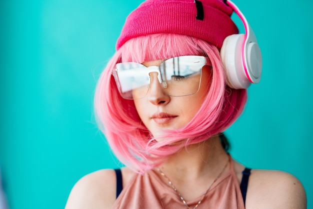 Uma adolescente de fones de ouvido com cabelo rosa uma menina com um corte de cabelo curto em um fundo azul