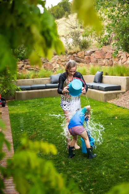 Uma adolescente e seu irmão brigando por água no jardim, esvaziando baldes de água