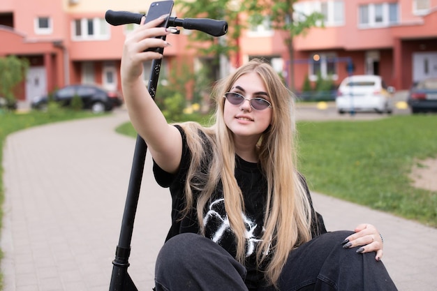 Uma adolescente em óculos de sol tira uma selfie em uma scooter