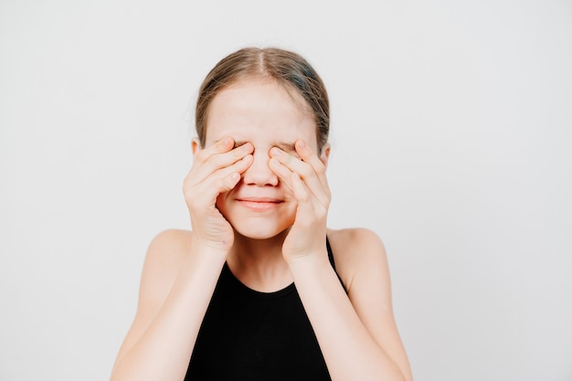 Uma adolescente em uma camiseta preta fecha os olhos com as mãos contra a parede branca. esperando uma surpresa ou relutância em ver. proibição de visualização para crianças.