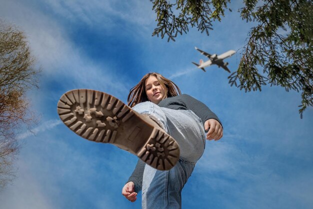 Foto uma adolescente está de pé com a perna erguida ao ar livre contra um céu azul com uma vista inferior de avião