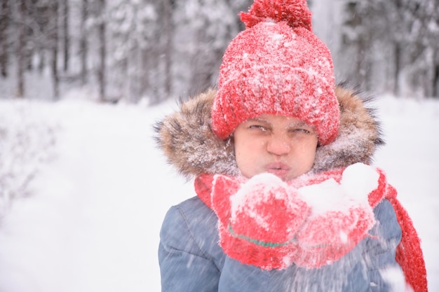 Uma adolescente está soprando na neve em suas palmas e abanando luvas e um chapéu de malha mudando o clima