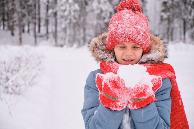 Uma adolescente está soprando na neve em suas palmas e abanando luvas e um chapéu de malha mudando o clima