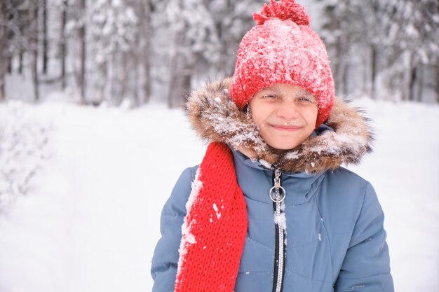 Uma adolescente está soprando na neve em suas palmas e abanando luvas e um chapéu de malha mudando o clima