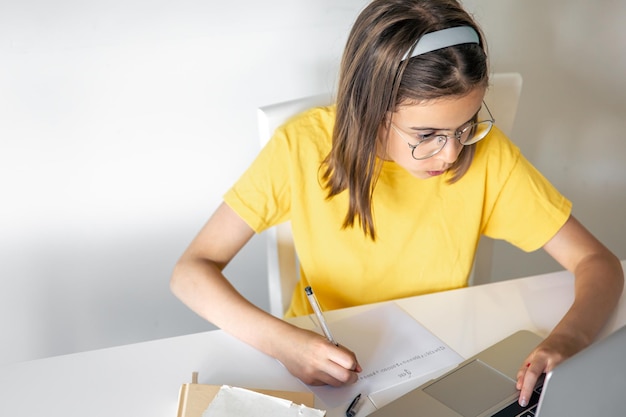 Uma adolescente faz sua lição de casa enquanto está sentada com livros e um laptop