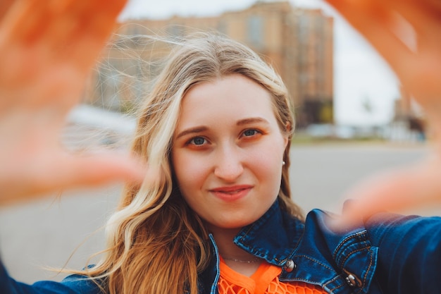 Uma adolescente legal tira uma selfie na rua Uma loira linda tira fotos de si mesma enquanto caminha pela cidade geração z