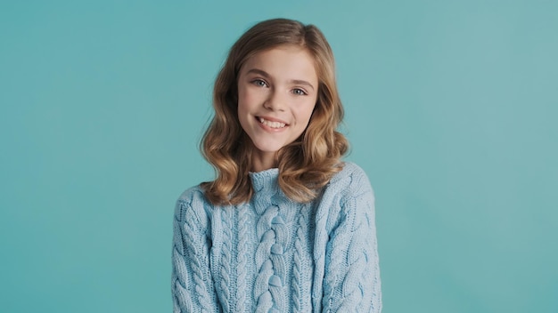 Uma adolescente loira e bonita com cabelos ondulados parecendo fofa sorrindo para a câmera sobre fundo azul