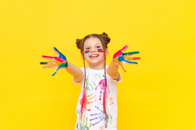 Uma adolescente manchada de tinta multicolorida mostra as palmas das mãos e sorri amplamente A arte do desenho para crianças em idade escolar Cursos de desenho à mão livre Cores da vida